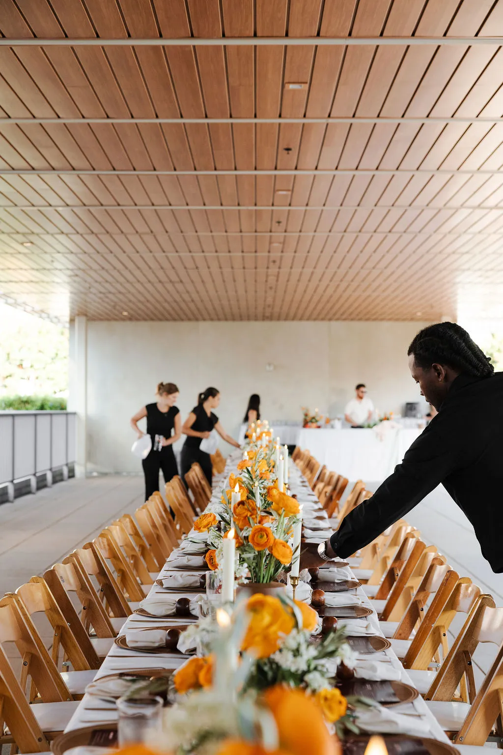 A long candlelit dinner table set with orange flowers for a Bosforo catered event