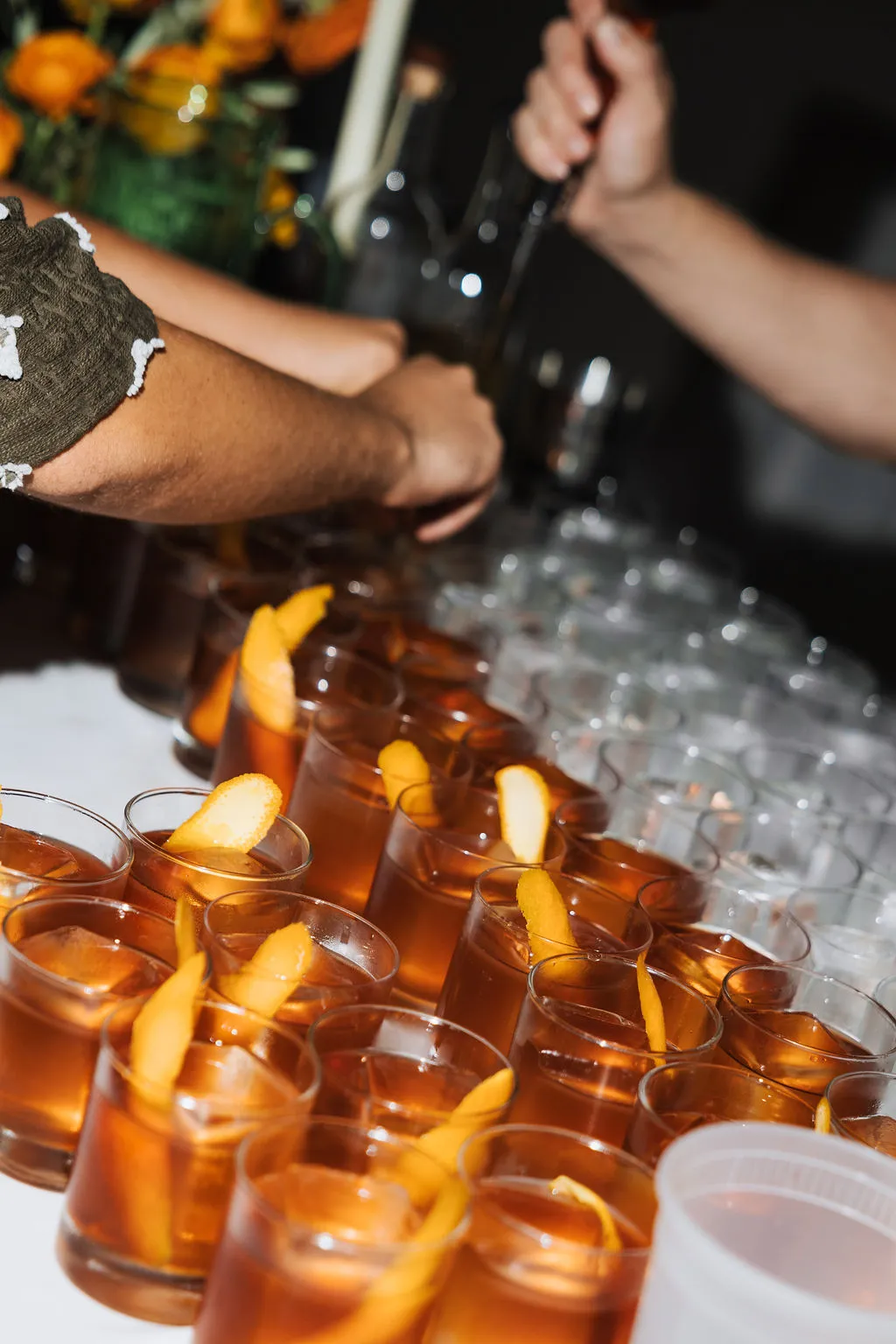 Rows of amber cocktails garnished with orange being finished at the bar